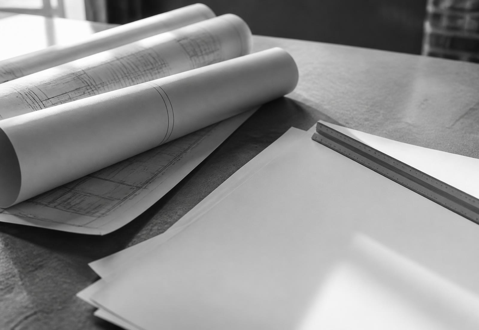Planos técnicos enrollados y una escala sobre una mesa de trabajo