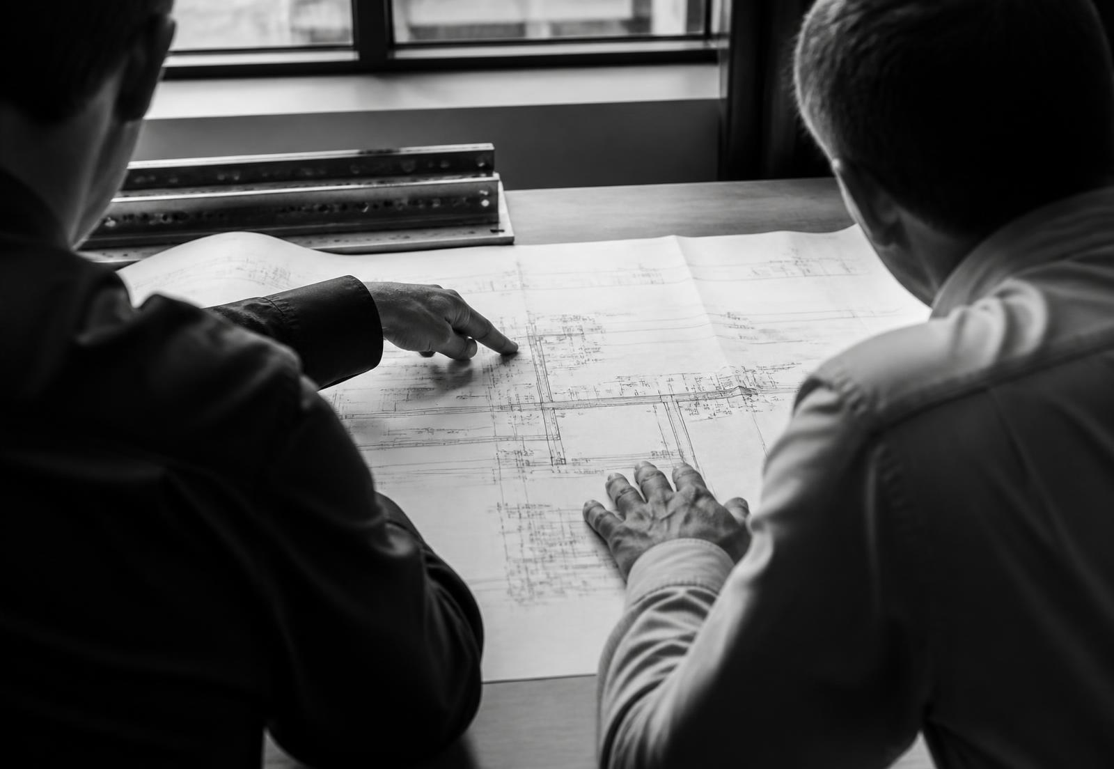 Dos profesionales de espaldas revisando un plano extendido sobre una mesa