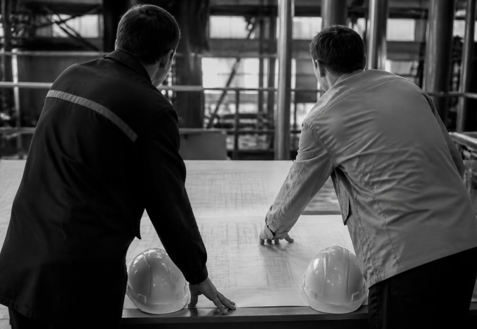 Dos especialistas revisan planos técnicos sobre una mesa en una instalación industrial.
