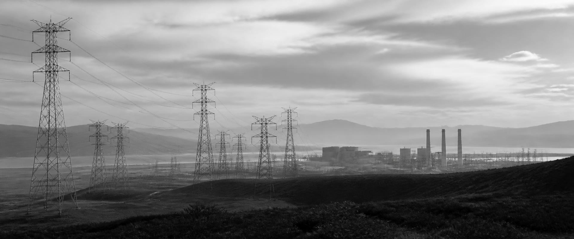 Infraestructura de transmisión e instalación de generación integradas en un paisaje abierto, fotografía en blanco y negro.